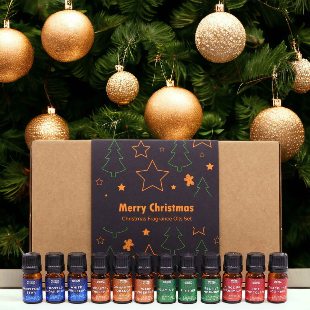 Set Delicias Festivas abierto con doce frascos de aceite aromático delante de un árbol de Navidad con bolas rojas y doradas